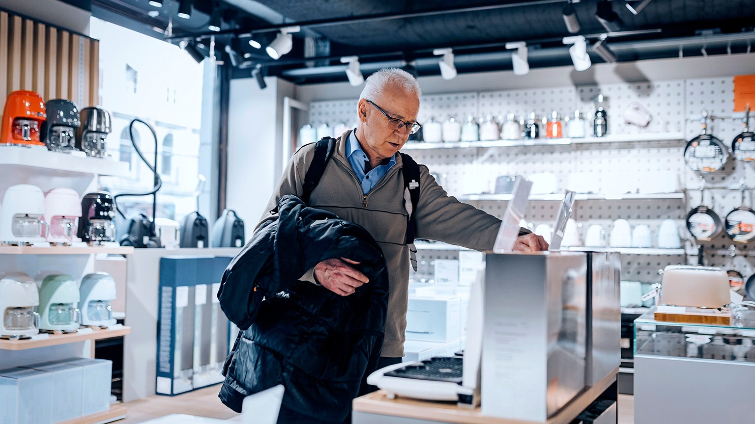 A mature man looking thoughtfully at an appliance at a home electronics store.